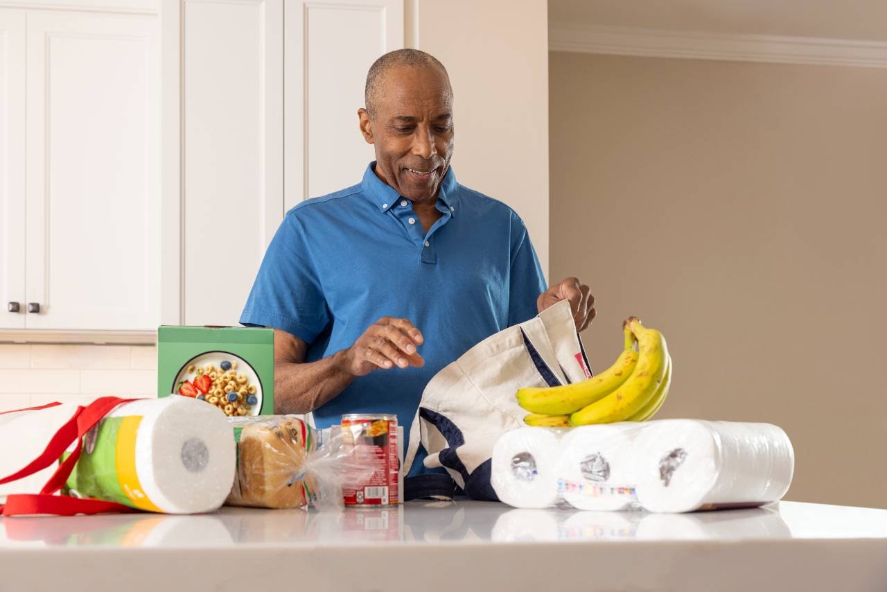 A gentleman in a blue shirt unloads groceries at his kitchen counter
