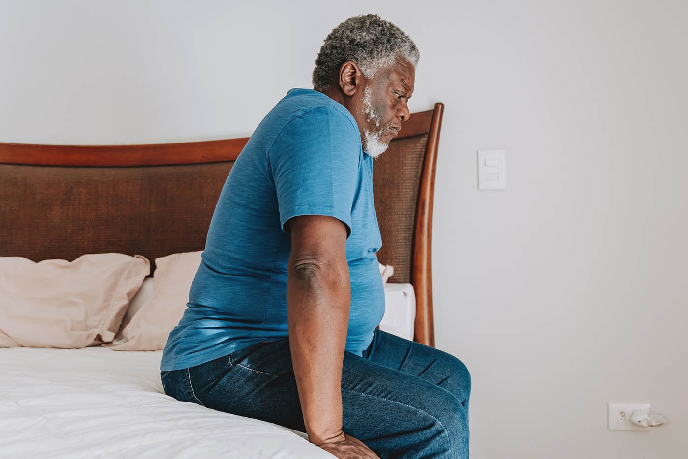 A mature gentleman sits on the edge of his bed