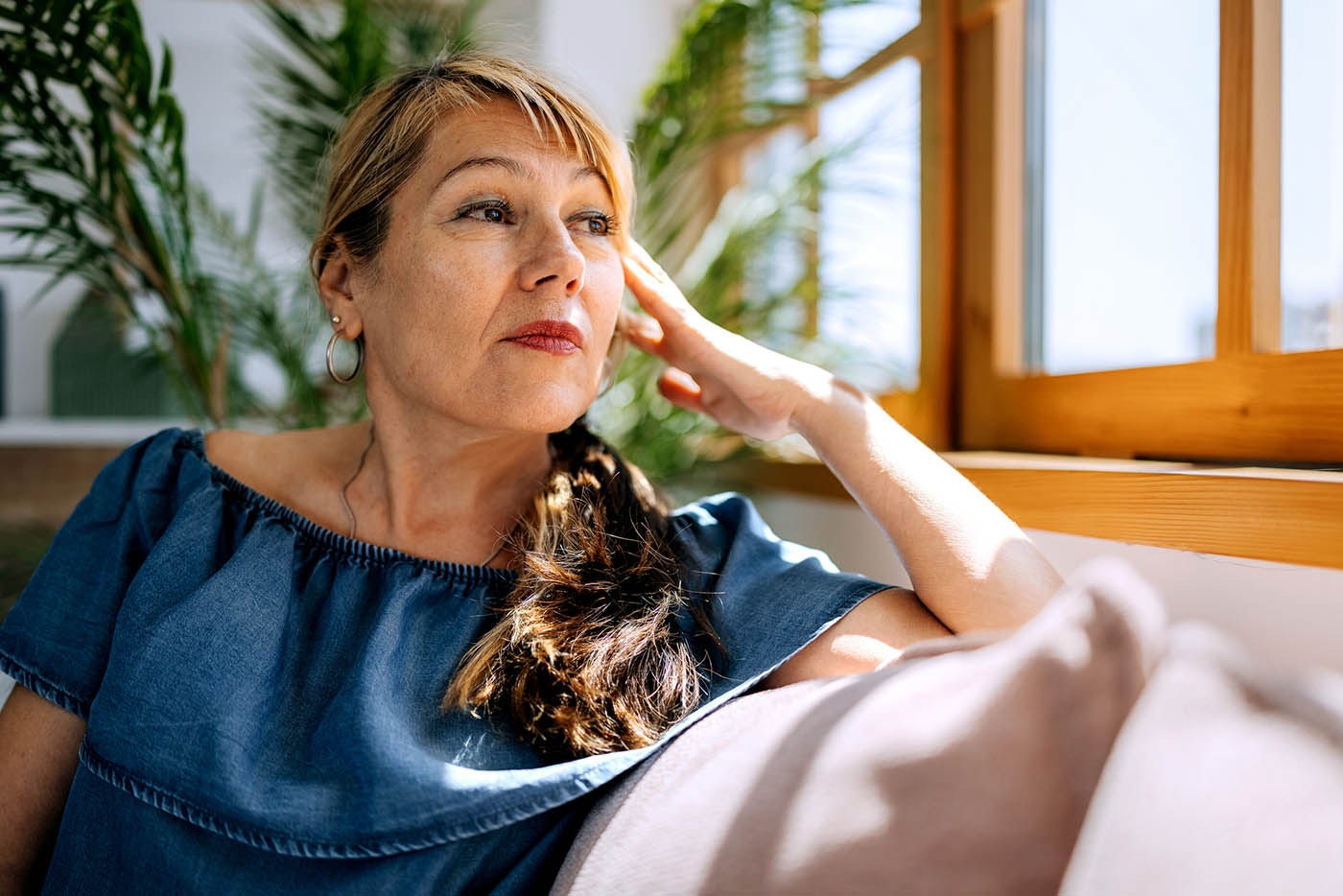 A mature woman sits on her couch looking out the window