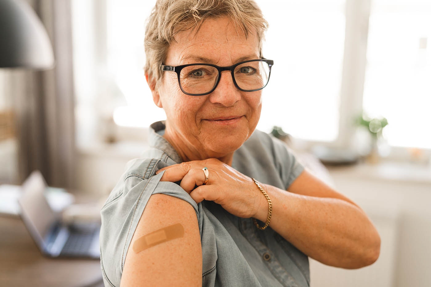 A senior woman that has received her flu vaccine. She is pulling up her sleeve to show the bandage.
